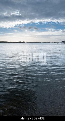 Bosham Harbour, West Sussex, England, bei Flut mit einem vertäuten Holzboot und einem überfluteten Damm-Schild unter einem hellblauen Himmel mit Wolken Stockfoto