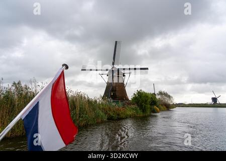 Historische Windmühlen entlang der Wasserstraße von einem Boot mit der niederländischen Flagge aus gesehen. Stockfoto