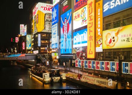 Ein Touristenboot, das entlang des Dotonbori-Kanals unter dem berühmten Glico man-Schild fährt Stockfoto