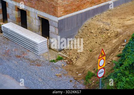 Die Arbeiter bereiten sich auf eine Baustelle vor, in der sich Materialien und Erde in der Nähe eines Gebäudes stapeln. Stockfoto