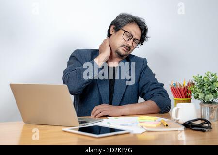 Junger asiatischer Mann, der an seinem Schreibtisch sitzt und seinen Hals und seine Schulter wegen stundenlanger Computerarbeit vor Schmerzen hält. Konzept des Office-Syndroms, Muscle tens Stockfoto