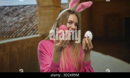 Eine junge Frau mit Hasenohren hält farbenfrohe ostereier in einem historischen Universitätsgebäude, in dem eine fröhliche, festliche Atmosphäre drinnen herrscht. Stockfoto