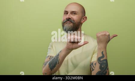 Kahler bärtiger Mann mit Tattoos Gesten mit Daumen vor gelber Wand isolierter Hintergrund Stockfoto