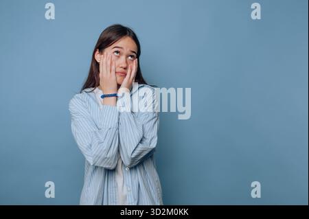 Junge Frau in gestreiftem Hemd, frustriert vor blauem Hintergrund. Stockfoto