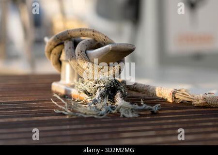 Das ausgefranste Seil ist sicher an einem Metallklammer an einem hölzernen Dock befestigt und reflektiert Festigkeit, Belastbarkeit und nautisches Erbe Stockfoto