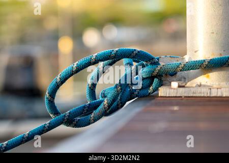 Sicher befestigtes blaues Seil, das um Metallpfoller auf hölzernem Dock gewickelt ist, Nautischer Knoten, der das Boot an Ort und Stelle hält Stockfoto