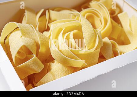 Rohe Pappardelle Nudeln, Nudelnester, in einem Papierkarton, hartes Licht, Blick von oben, keine Leute Stockfoto