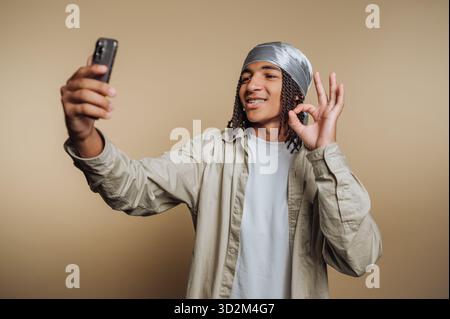 Ein junger Mann macht ein Selfie mit einem Smartphone und macht ein OK-Zeichen. Stockfoto