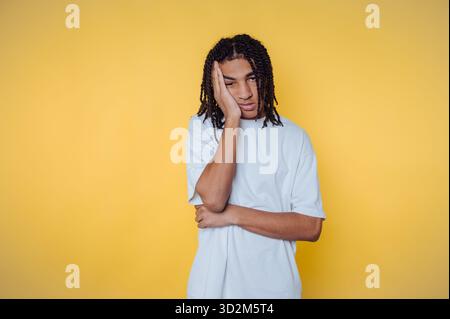 Junger Mann mit Dreadlocks in weißem Hemd, der auf gelbem Hintergrund langweilig aussieht. Stockfoto
