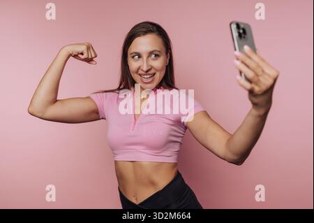 Frau in rosa Oberteil, die ein Selfie macht, während sie ihren Arm beugt. Stockfoto