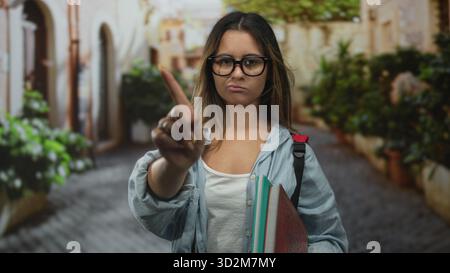 Frau zeigt den Finger in der Straße nach vorne, hält Notizbücher und Rucksack, während sie Brille und Jeansshirt trägt; Bestimmungsgrenze. Stockfoto