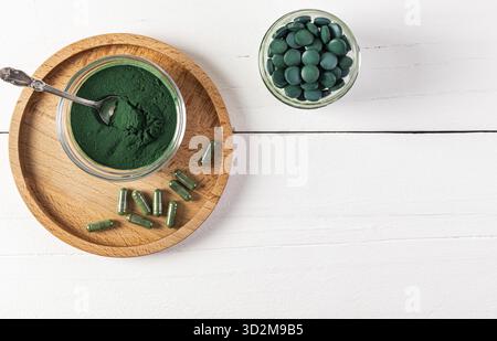 Natürliches Organisches Grünes Spirulina-Algenpulver Im Glas, Runde Tabletten, Kapseln Auf Hölzernem Runden Tablett Und Weißem Hintergrund. Draufsicht Stockfoto