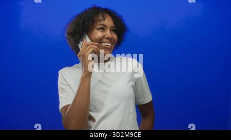 Frau lächelt natürlich und hält das Smartphone im Studio an das Ohr; positiver Optimismus bei Gesprächsverbindungen. Stockfoto