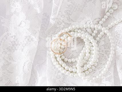 Zwei goldene Eheringe liegen auf einem luxuriösen Vintage-Teil des Hochzeitskleides der Braut mit einer Perlenschnur. Hochzeitskonzept. Draufsicht Stockfoto