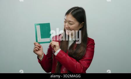 Lächelnde Frau, die ein Lernzeichen in roter Jacke auf weißem Hintergrund hält, das Begeisterung und Lernkonzept für pädagogische oder motivierende Themen zeigt Stockfoto