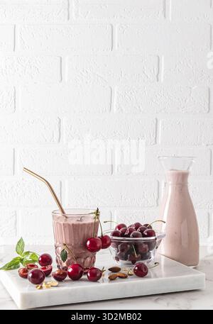 Schöner vertikaler Look eines Stilllebens mit einem köstlichen, gesunden Kirsch-Smoothie in einer Flasche und einem Glas mit umweltfreundlichem Strohhalm. Reife Beeren Stockfoto