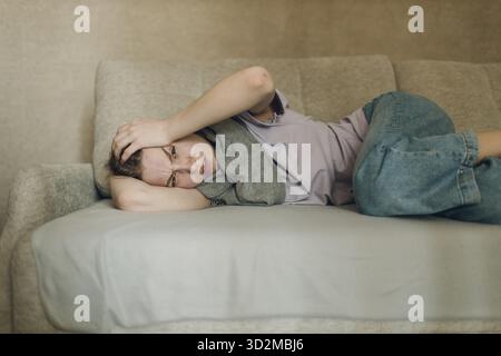 Junge Frau mit Schal hat Grippe krank krank Krankheit kalt zu Hause drinnen liegen auf dem Sofa Stockfoto