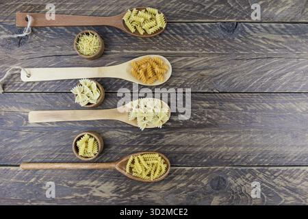 Holzlöffel und Holzschüsseln mit trockenen italienischen Nudeln in verschiedenen Formen auf einem rustikalen braunen Tisch. Draufsicht Stockfoto