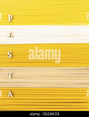 Ein Hintergrund mit trockenen langen Nudeln, Nudeln und Spaghetti mit einem Wort aus Holzbuchstaben - Pasta. Draufsicht. Flache Lagen Stockfoto