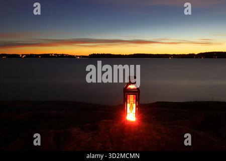 Eine rote und gelbe Laterne in der Nacht. Gemütliches Abendlicht von der Kerze. Der Mälarensee im Hintergrund. Järfälla, Schweden. Stockfoto