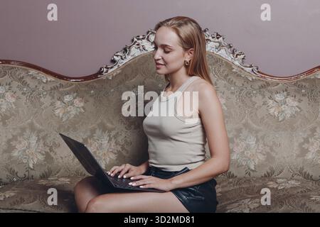 Junge Frau mit blonden Haaren sitzt und verwenden Laptop auf der Couch Stockfoto