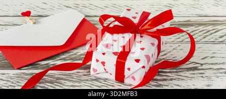 Valentinstag Geschenkbox mit Umschlag mit Liebesbrief, Papierherzen auf Holzhintergrund. Grußkarte für Valentinstag oder Geburtstag Stockfoto