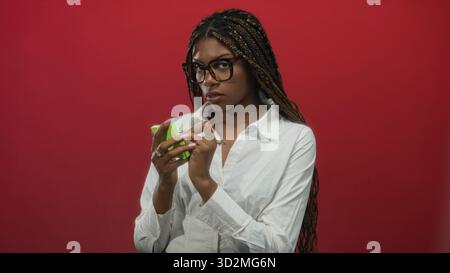 afroamerikanerin schreibt mit Stift auf grüne Haftnotizen, Hände über Notizen, posiert vor rotem Studio-Hintergrund; Konzentrationsplanung. Stockfoto