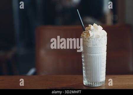 Vanillemilchshake mit einem Strohhalm in einer Glastasse auf dem Tisch Stockfoto