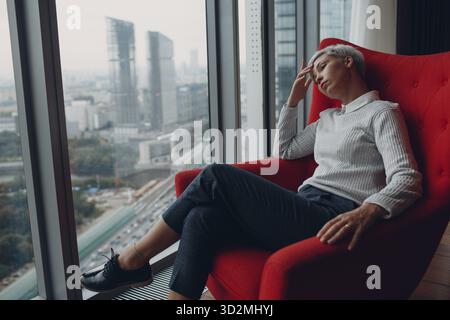 Eine junge Frau sitzt im Stuhl am Fenster zu Hause. Bleib zu Hause und Quarantäne Stockfoto