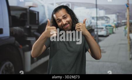 Mann mit langen dunklen Haaren und Bart lächelt, während er auf einer belebten Straße neben einem geparkten Truck und Bürgersteig zwei Daumen nach oben zeigt; Optimismus. Stockfoto