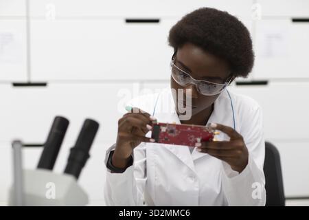 Wissenschaftlerin afroamerikanerin, die im Labor mit elektronischer Platine arbeitet. Forschung und Entwicklung durch die farbige schwarze Frau Stockfoto