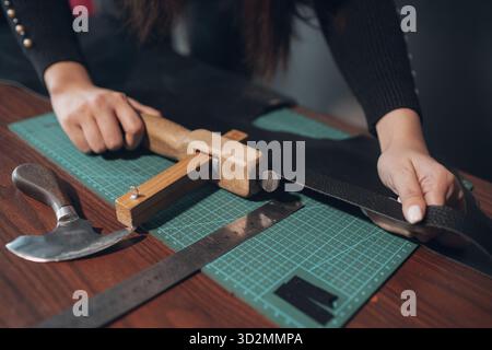 Tanner Frau schneidet Lederwaren in der Werkstatt. Arbeitsprozess des Lederhandwerks Stockfoto
