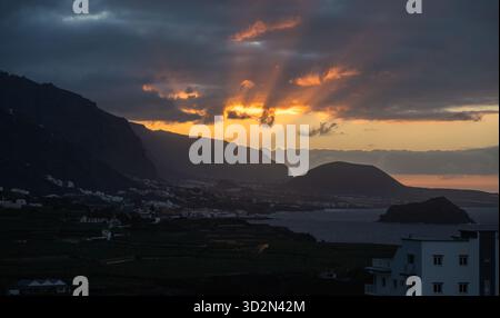 Blick auf den Sonnenuntergang über die Küstenstadt Garachico und die umliegenden Bananenplantagen von San Marcos aus mit goldenem Licht, das durch mountai strömt Stockfoto