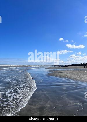 Gilan, Iran – Strand am Kaspischen Meer mit sanfter Brandung und spiegelähnlichem nassem Sand unter einem hellblauen Himmel mit verstreuten Kumuluswolken. Stockfoto