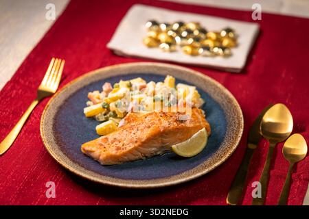 Teller mit gebratenem Lachs und Kartoffelsalat auf roter Tischdecke Stockfoto