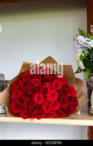 Herzförmiger Blumenstrauß aus leidenschaftlichen roten Rosen, verpackt in Kraftpapier auf einem Holzregal Stockfoto
