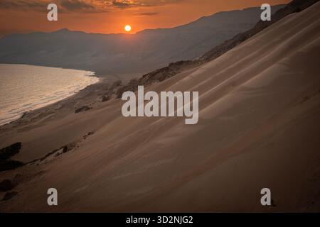 Ein wunderschöner Sonnenuntergang färbt den Himmel orange, während er über den ruhigen Sanddünen nahe der Küste von Socotra im Jemen untergeht und eine friedliche Szene schafft. Stockfoto