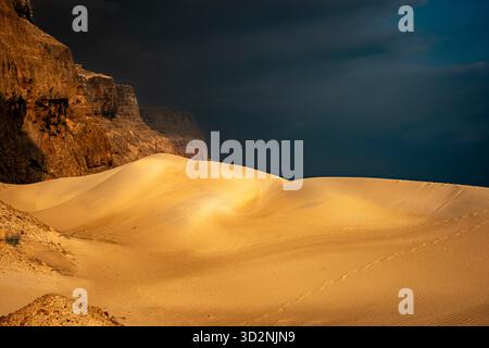 Genießen Sie die ruhige Schönheit der goldenen Sanddünen von Socotra, die auf zerklüftete Klippen treffen, die während der Dämmerung vor einem stimmungsvollen Himmel liegen. Stockfoto