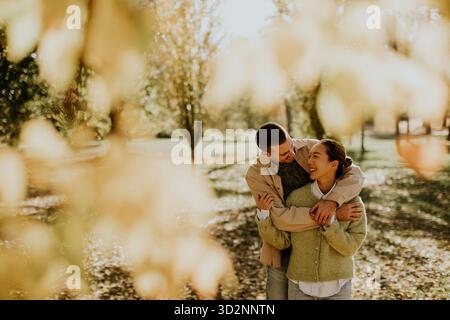 Während der goldenen Stunden des Tages lacht ein Paar und ist von lebhaften Herbstblättern umgeben. Stockfoto
