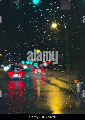Künstlerische Sicht auf sich bewegende Autos und Stadtlichter durch Regentropfen auf einer Windschutzscheibe während einer regnerischen Nacht in Edmonton, Alberta, Kanada Stockfoto
