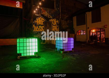 Zwei leuchtende Kunststofftanks mit Neonbeleuchtung im mit Graffiti bedeckten Innenhof bei Nacht, die kreative Street Art-Umgebung mit industria darstellen Stockfoto