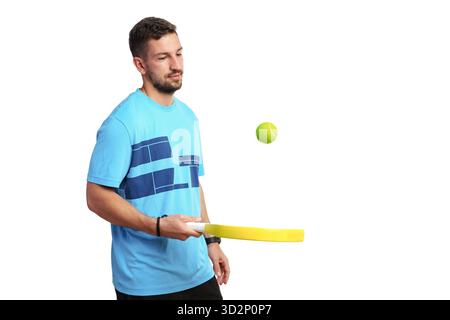 Junger Mann, der drinnen mit einem gelben Paddel und Tennisball spielt Stockfoto