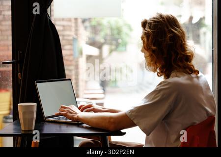 Junge Person, die an einem regnerischen Tag in einem Café an einem Laptop arbeitet Stockfoto