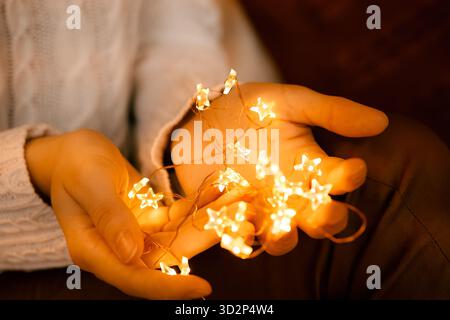 Ein Mädchen in einem weißen Pullover hält eine Sternenkranz in den Händen. Silvester-Atmosphäre, Vorfreude auf den Urlaub, Wünsche Stockfoto