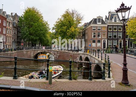 Kanalboote, die unter der historischen Brücke im Stadtzentrum von Amsterdam vorbeifahren Stockfoto