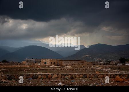 Wolken sammeln sich über den Gebirgszügen von Socotra, Jemen, und werfen Schatten auf die historischen Gebäude und das raue Gelände darunter. Stockfoto