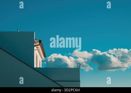 Minimalistische moderne Gebäudefassade vor klarem blauem Himmel, helles Sonnenlicht und flauschige Wolken schaffen eine klare geometrische Komposition. Selektiver Fokus. Stockfoto