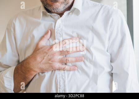 Geschäftsmann in weißem Hemd leidet unter starken Brustschmerzen, Nahaufnahme des Mannes, der seine Brust wegen plötzlicher Herzschmerzen klammert, Notfall-Gesundheitskonzept. S Stockfoto