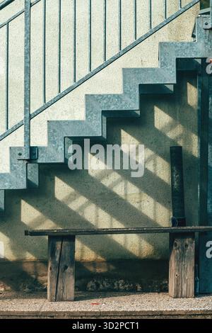 Holzbank und Metalltreppe auf einem Bauernhof, rustikale ländliche Szene mit funktionellen Sitzgelegenheiten im Freien und architektonischen Details. Vertikales Bild. Stockfoto