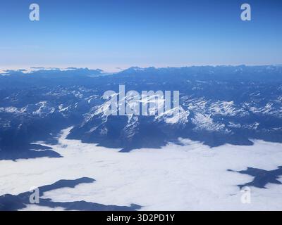 Aus der Vogelperspektive auf eine schneebedeckte Bergkette, die sich über einem Wolkenmeer unter einem klaren blauen Himmel erhebt. Riesige, dramatische alpine Landschaft, perfekt für Reisen Stockfoto